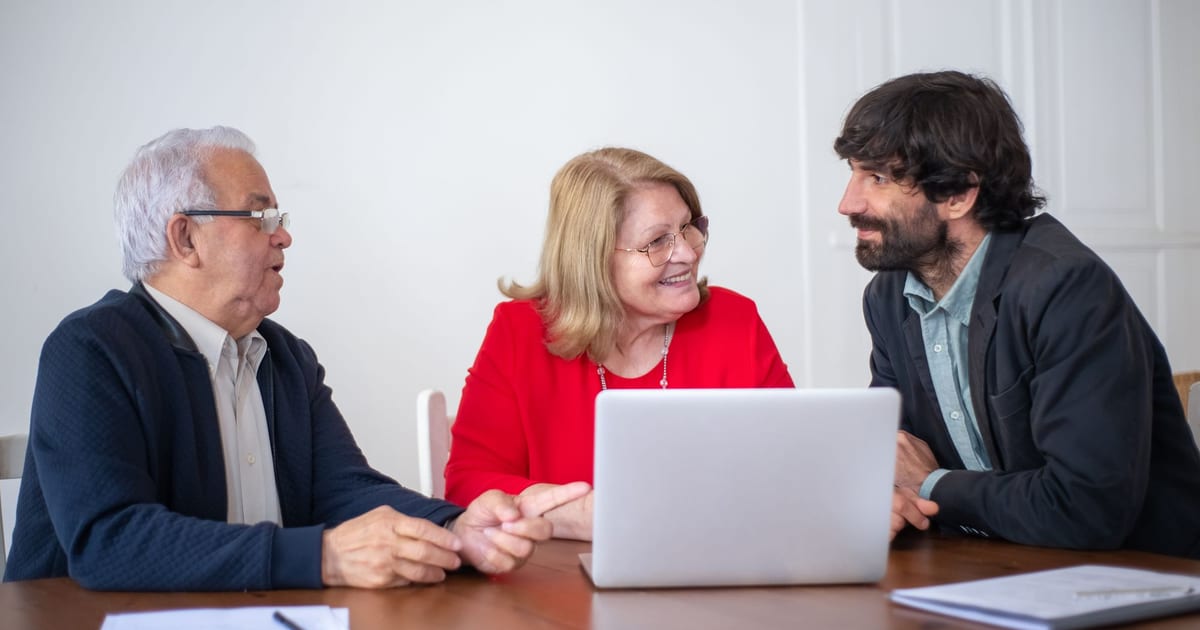 An advisor talking with an older couple across a table with a laptop open